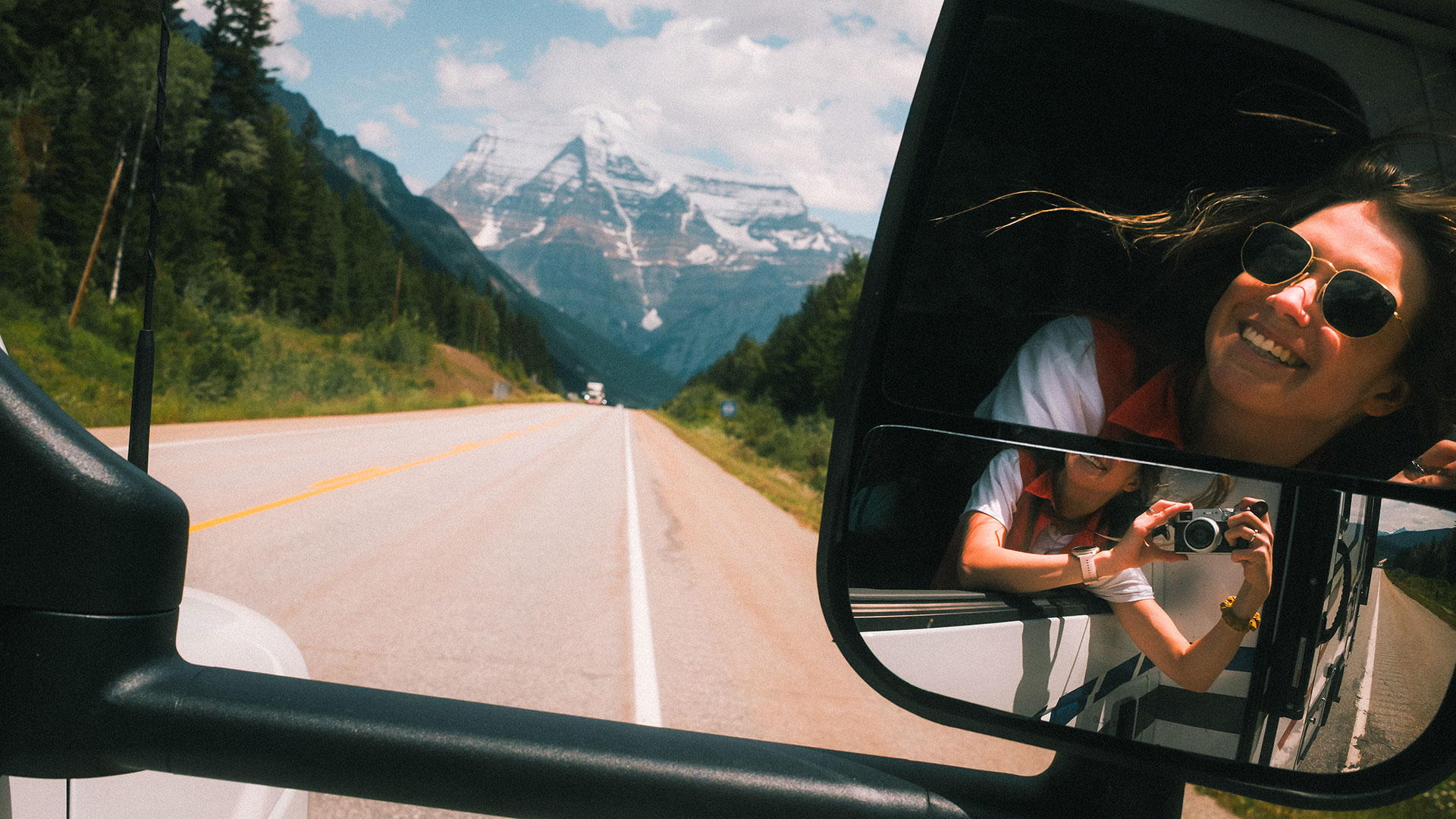 Glade rejsende fanger øjeblikket med bjergene i baggrunden - canadisk eventyr set fra sidespejlet.