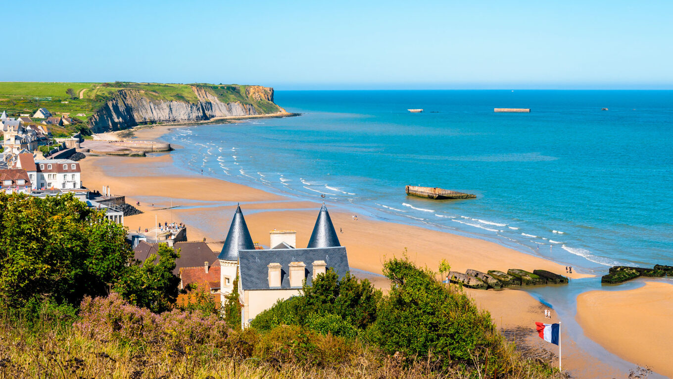 Kystudsigt med strand, klipper og ruiner fra D-dag ved Arromanches i Normandiet