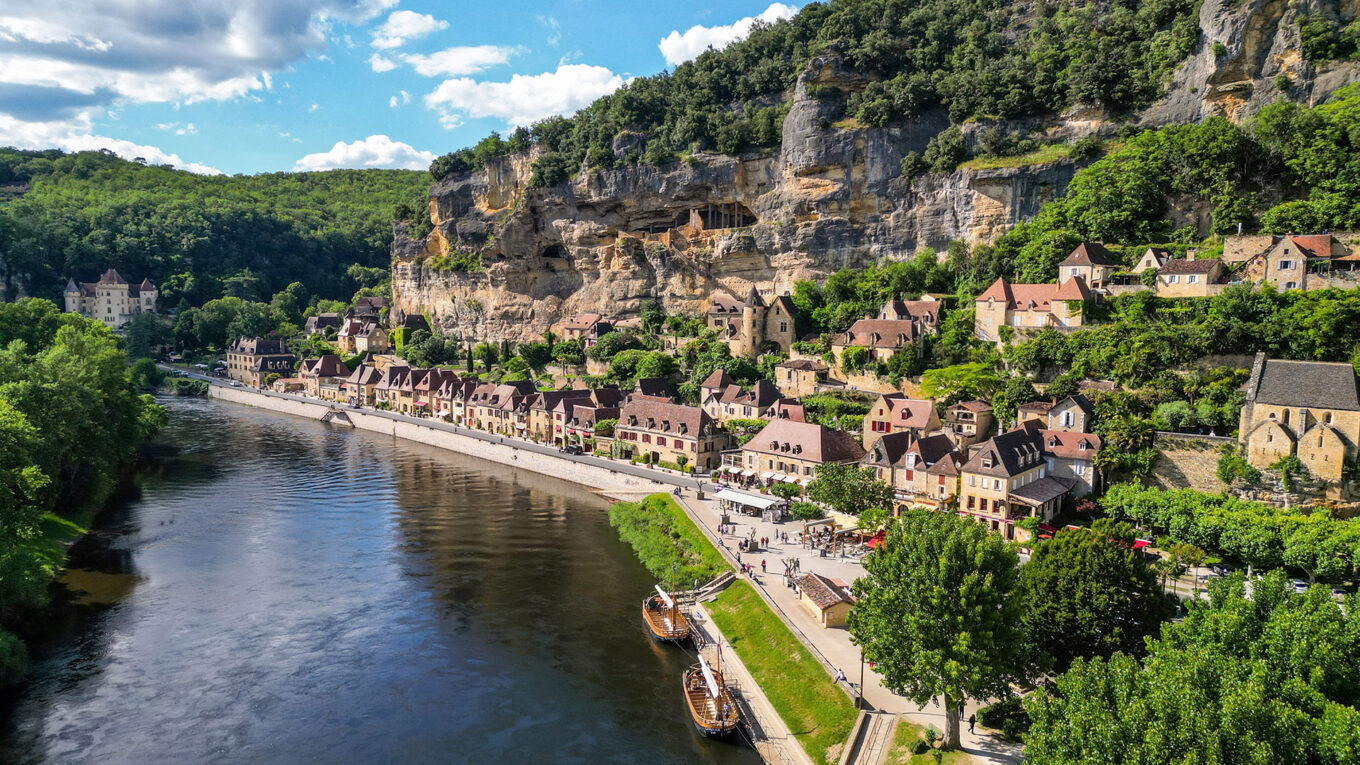 Udsigt til La Roque-Gageac langs Dordogne-floden med klippevæg og både