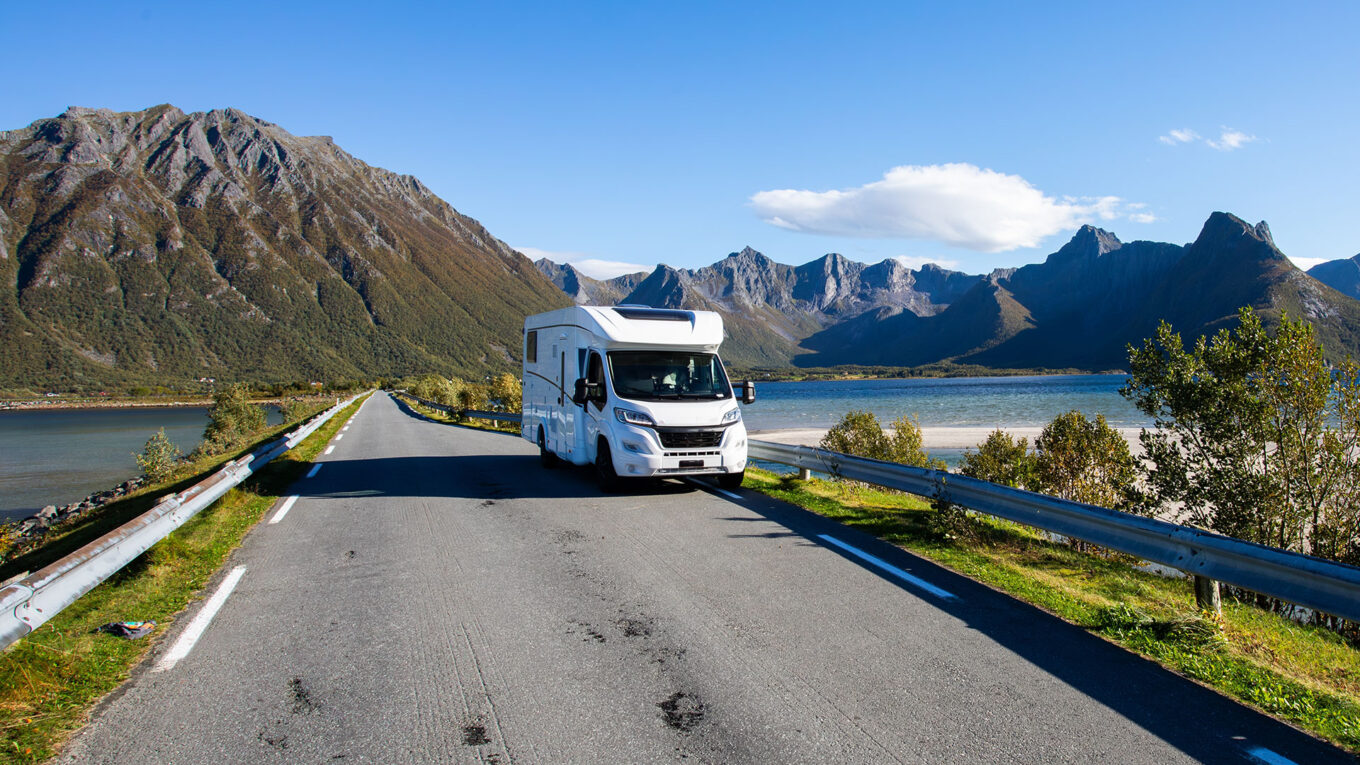 Autocamper parkeret ved en idyllisk norsk sø omgivet af frodige fjelde og grøn natur.
