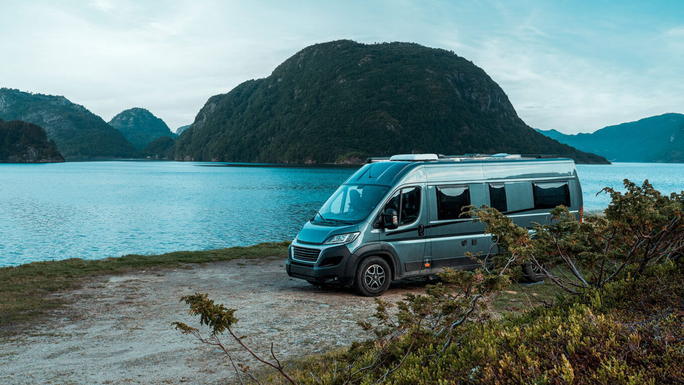 Autocamper parkeret ved en idyllisk norsk sø omgivet af frodige fjelde og grøn natur.