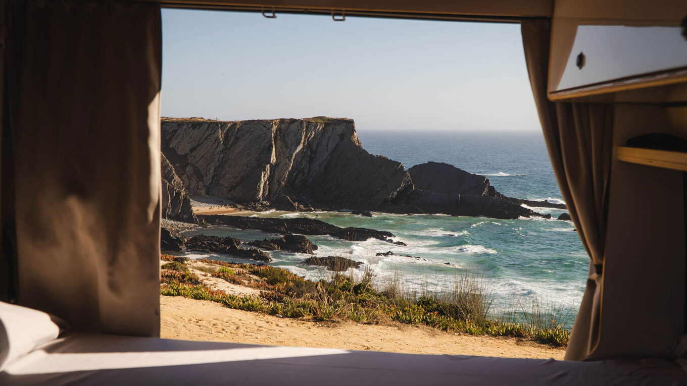 Udsigt fra seng i autocamper til rå klippekyst og bølger i Portugal