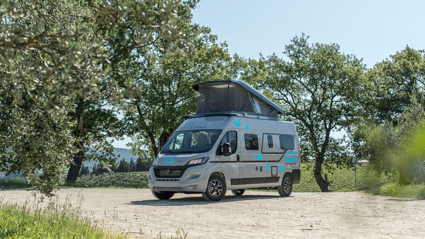 Moderne campervan med pop-op tag parkeret under grønne træer i det engelske landskab – ideelt valg til fleksible autocamperrejser i Storbritannien.