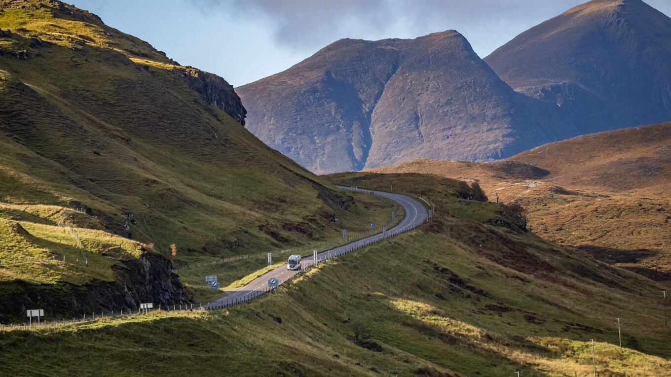Autocamper kører ad snoet vej mellem skotske bjerge – en klassisk oplevelse på North Coast 500 ruten i det nordlige Skotland.