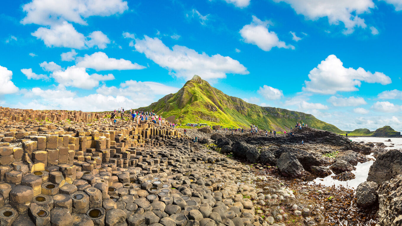 Turister går på de ikoniske sekskantede klippeformationer ved Giant’s Causeway – en uundgåelig seværdighed på en autocampertur i Nordirland.