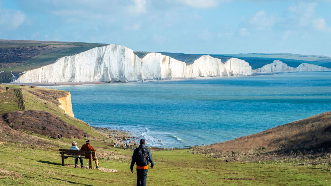 En mand går mod de hvide klipper ved Seven Sisters på Englands sydkyst – perfekt til vandring undervejs på autocamperferien.