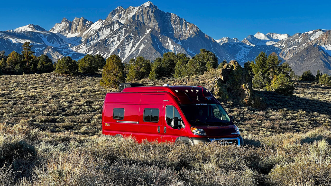 Class B autocamper kører gennem snoede bjergveje i Rocky Mountains med sneklædte tinder og skovlandskab – perfekt til eventyr i USA.