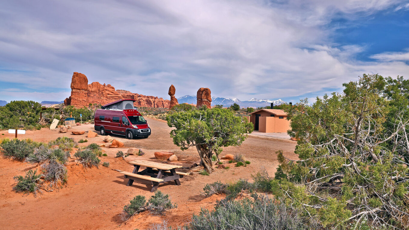 Rød autocamper camperer i Arizonas ørkenlandskab med unikke klippeformationer i baggrunden – oplev friheden på fire hjul i USA.